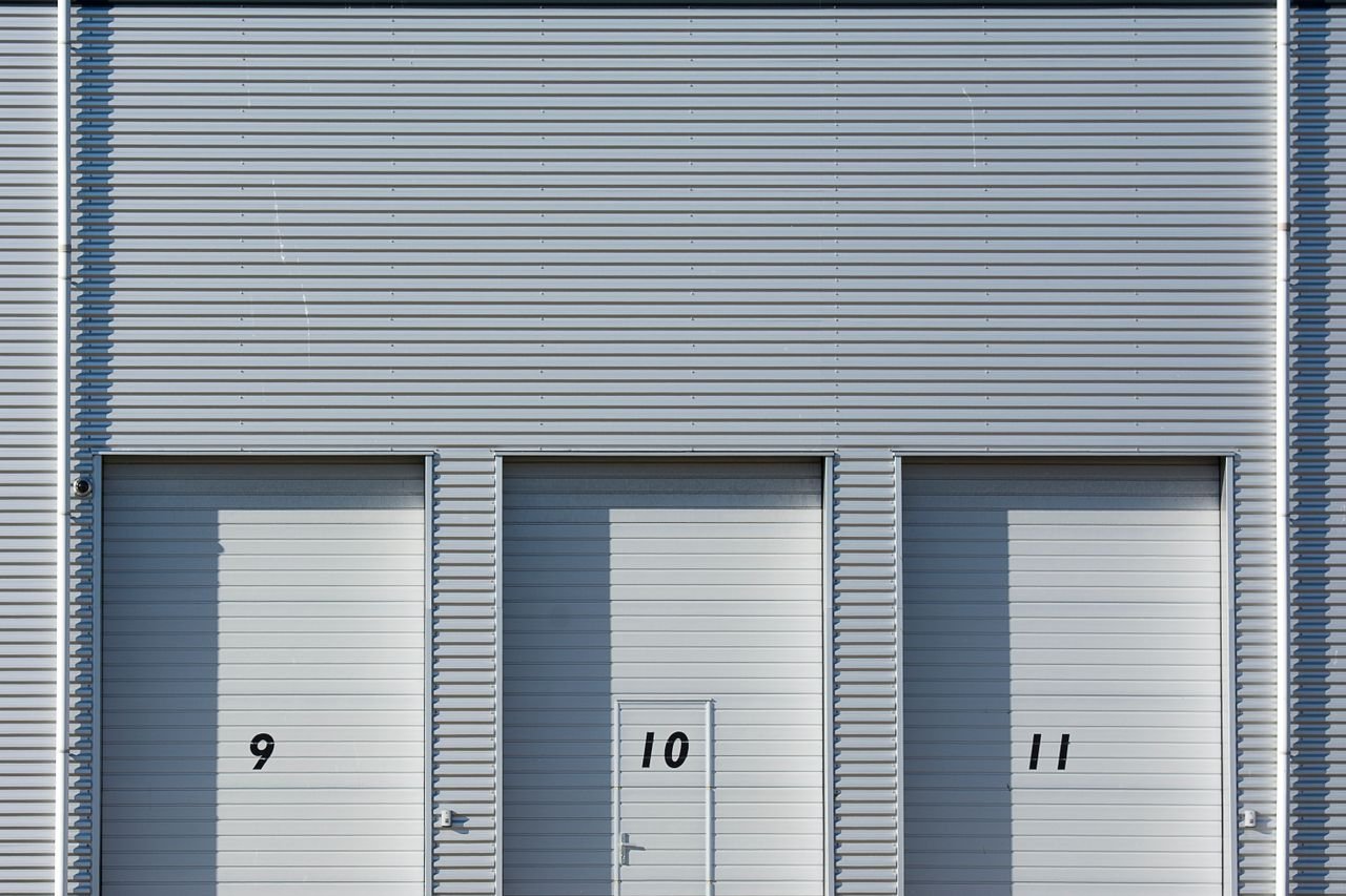 Home Close-up view of a modern industrial building with metal shutters numbered 9, 10, and 11, showcasing minimalist architecture.