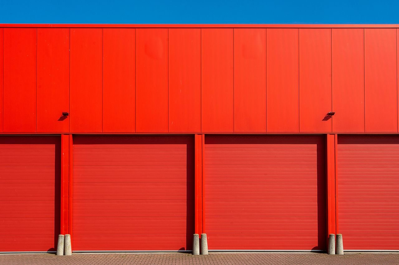 Bright red industrial garage doors in a modern building facade under a clear blue sky.